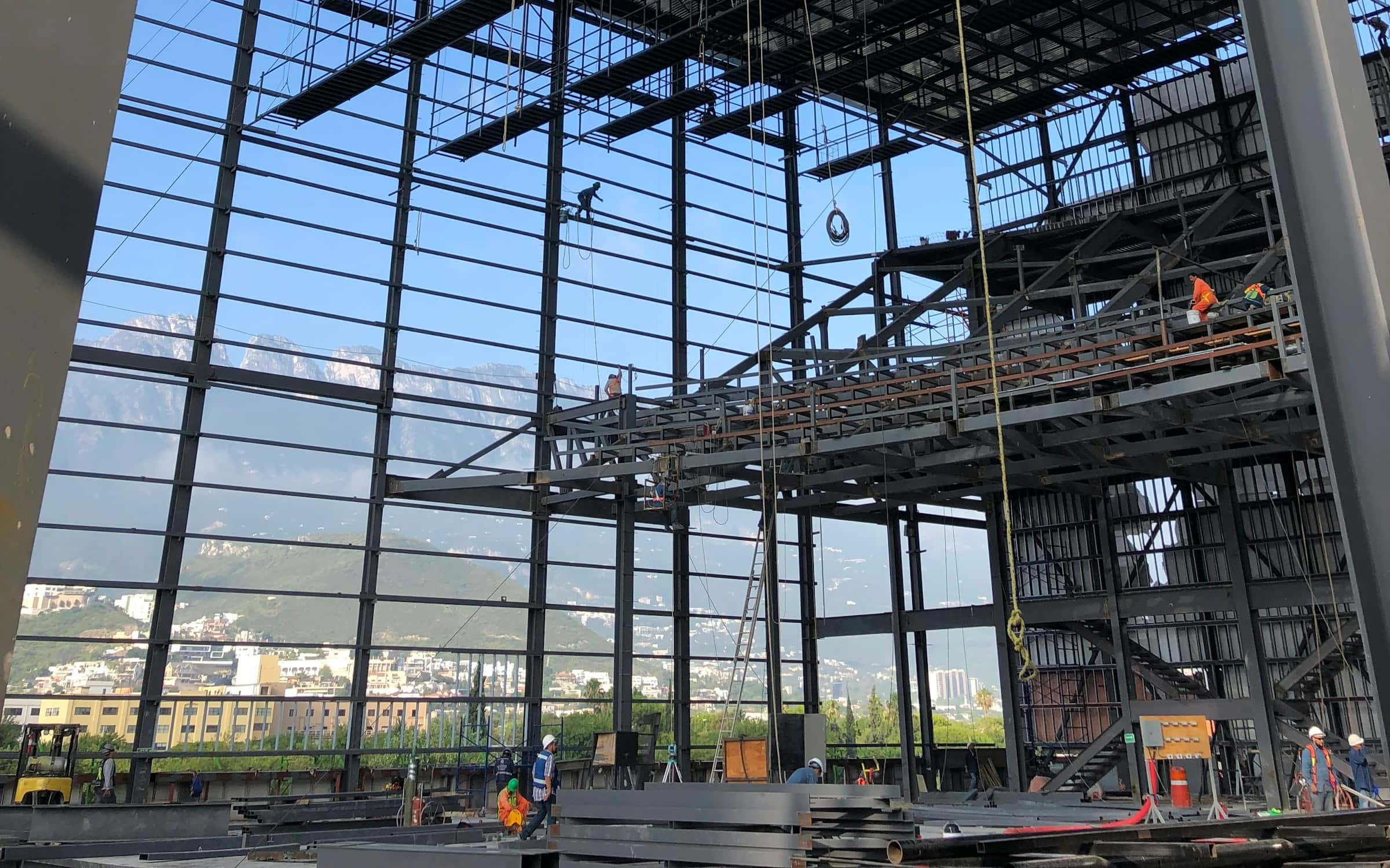 Structural steel frame under erection, floor decking being set overhead.