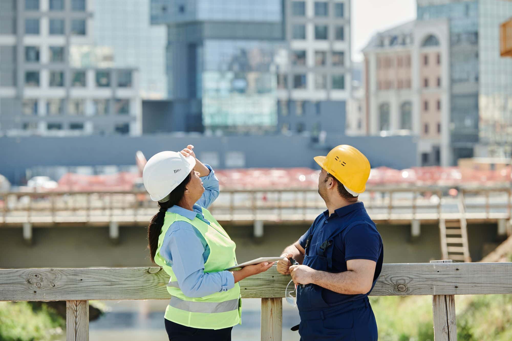 Two workers in hard hats and high-visibility gear on an active construction site.